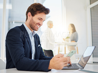 One young caucasian businessman browsing on a laptop and sending texts on a cellphone in an office. Confident entrepreneur planning and doing banking on his digital wireless devices