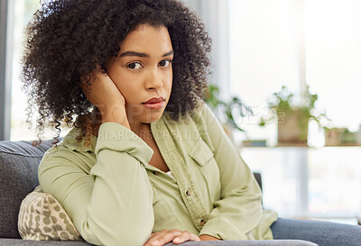 Young mixed race woman sitting on the couch alone at home. One unhappy hispanic female looking bored sitting at home. Woman with a curly afro sulking in the lounge at home