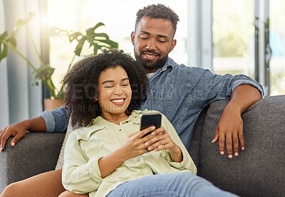 Buy stock photo Happy mixed race couple smiling while using a phone together at home. Carefree loving hispanic boyfriend and girlfriend bonding and using social media on a cellphone in the lounge at home