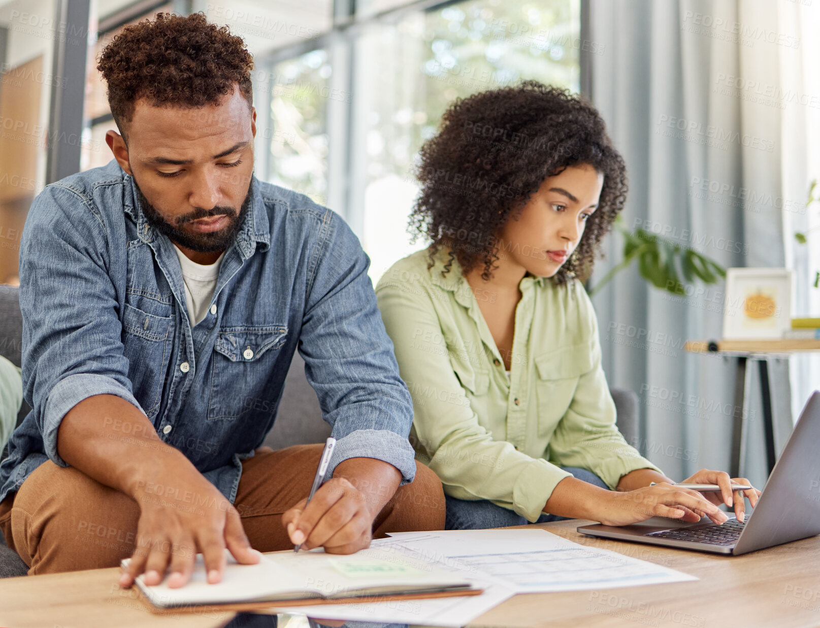 Buy stock photo Young mixed race couple going through bills and using a laptop at a table together at home. Husband and wife planning and working on their finances together