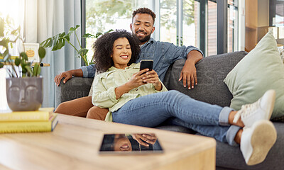 Buy stock photo Happy young mixed race couple smiling while using a phone together at home. Cheerful hispanic boyfriend and girlfriend bonding and using social media on a smartphone in the lounge at home