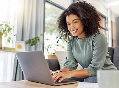 Buy stock photo Young mixed race woman working on filling out forms while typing on a laptop at home. One hispanic female smiling while planning and sending an email alone in the lounge at home