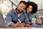 Young happy mixed race couple going through documents and using a laptop at a table together at home. Hispanic husband and wife planning and paying bills