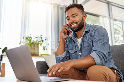 Buy stock photo Young mixed race man on a call using a phone while typing an email on a laptop at home. One hispanic man planning and working on a laptop alone in the lounge at home