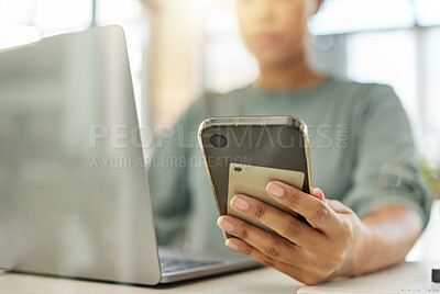 Buy stock photo Closeup of a mixed race woman holding a phone in her hand while working on a laptop at home. One hispanic female using social media on a cellphone while sending an email alone in the lounge at home