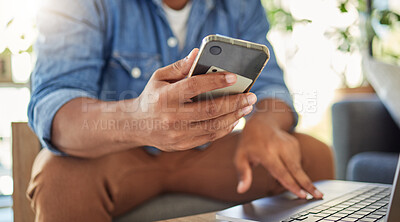 Hands of a freelance businessman using his laptop and cellphone. Closeup of entrepreneur sending a text on his smartphone. Businessman working from home on his wireless device.