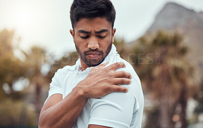 One indian tennis player suffering from bad shoulder injury during a game on court. Ethnic fit professional in pain while holding and rubbing arm after match. Sporty man standing alone in sports club