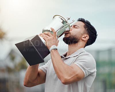 Mixed race tennis player drinking from trophy while celebrating success after winning court game. Hispanic fit athlete holding prize award after a match. Active healthy man playing competitive sport