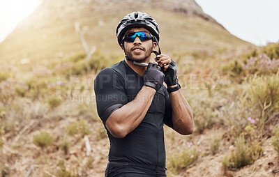 Buy stock photo One fit and active indian man wearing sunglasses and adjusting his helmet to cycle for an outdoor workout. Serious mixed race athlete getting ready to exercise in nature. Focused on health and cardio