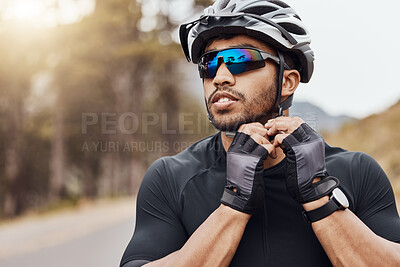 Buy stock photo Athletic sportsman wearing glasses and gloves while tying his cycling helmet. Male cyclist putting on a helmet for safety. Professional cyclist getting ready for a ride on a mountain road