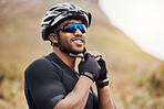 Smiling sportsman wearing glasses and gloves while tying his cycling helmet. Male cyclist putting on a helmet for safety. Professional cyclist getting ready for or finishing a ride on a mountain trail
