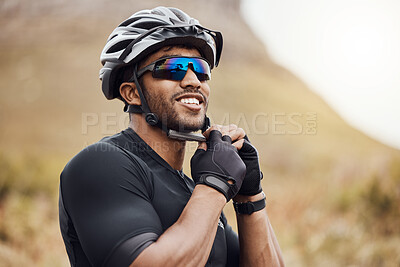 Buy stock photo Smiling sportsman wearing glasses and gloves while tying his cycling helmet. Male cyclist putting on a helmet for safety. Professional cyclist getting ready for or finishing a ride on a mountain trail