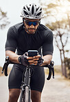 Male cyclist wearing helmet and glasses while using his smartphone and sitting on his bike. Fit sportsman using mobile phone while cycling outdoors