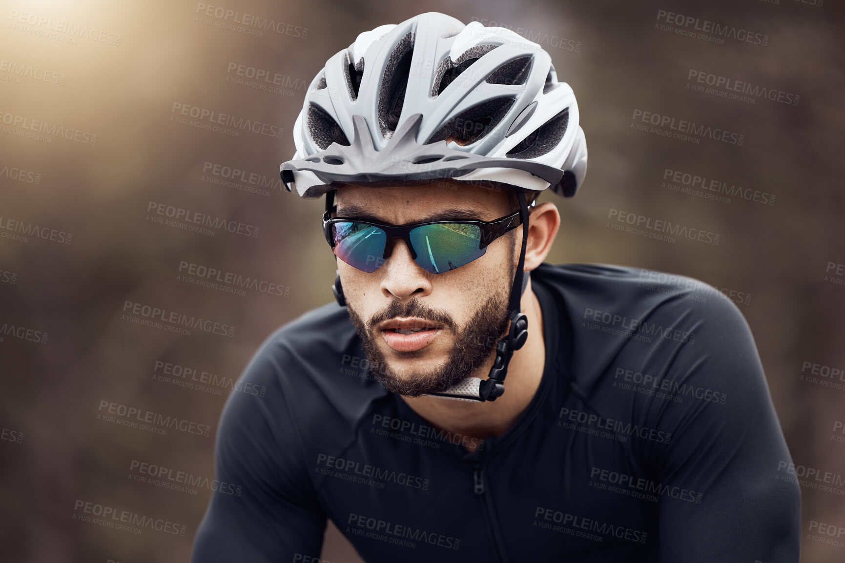 Buy stock photo Closeup of one athletic young man cycling outside. Serious guy wearing helmet and glasses while riding a bike for exercise or competition race. Endurance and cardio during a workout and training