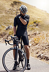 Male cyclist holding his shoulder in pain while suffering from a sports injury while cycling or training on a mountain road. Fit and active man wearing sports gear while exercising