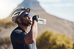 Close up of male cyclist taking a break and drinking water from a bottle. Fit young man wearing glasses and a helmet while drinking water and standing outside. Athletic man training in nature environment 
