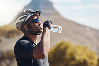 Buy stock photo Close up of male cyclist taking a break and drinking water from a bottle. Fit young man wearing glasses and a helmet while drinking water and standing outside. Athletic man training in nature environment 