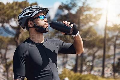 Buy stock photo Thirsty male cyclist taking a break and drinking water from a bottle. Fit young man wearing glasses and a helmet while drinking water and standing outside. Athletic man cycling in nature environment
