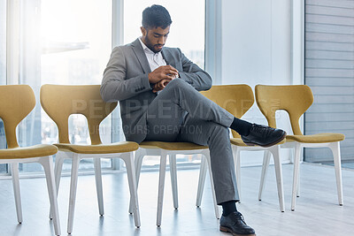 Buy stock photo Young indian businessman wearing suit checking the time on his watch while sitting and waiting in line on a chair for interview. Guy getting impatient for job vacancy meeting. Punctuality is important