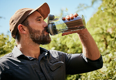 Close up of fit man drinking from a water bottle while out hiking. Fit and active male enjoying a trek, exercise and adventure while exploring the beauty of nature alone