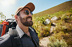 Fit adventurous man wearing glasses cap and a backpack while out hiking or exploring by the mountains. Handsome man with beard smiling while exploring nature on a sunny day
