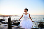 Elegant young ballerina wearing white fancy dress while leaning against a railing on the promenade with a beautiful ocean background at sunset