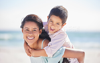 Portrait of a mixed race boy laughing while enjoying a piggyback ride on his mothers back at the beach. Mom and son enjoying a summer vacation by the sea. Enjoying family time while on holiday