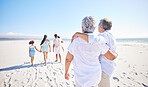 Rear view of senior couple enjoying a beach vacation with their family. Grandma and grandpa walking together while younger generation walks ahead and enjoy outdoor activity