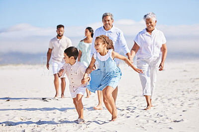 Buy stock photo Little girl and boy holding hands while running together on sandy beach while parents and grandparents follow in the background. Carefree sibling brother and sister having fun during summer beach vacation with their family