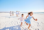 Adorable little girl and boy running together on sandy beach while parents follow in the background. Carefree sibling brother and sister having fun during summer beach vacation with their family. Multi generation family enjoying outdoor activity by the se