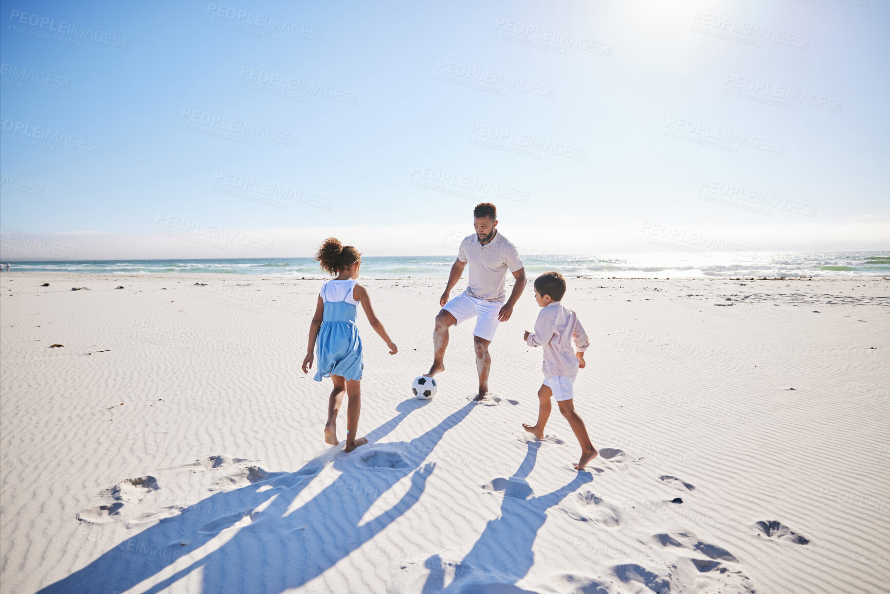 Buy stock photo Carefree father and two children playing soccer on the beach. Single dad having fun and kicking ball with his little daughter and son while on vacation by the sea