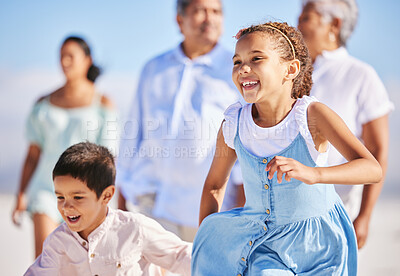 Excited little girl and boy running together on sandy beach while parents follow in the background. Carefree sibling brother and sister having fun during summer beach vacation with their family. Multi generation family enjoying outdoor activity by the sea