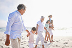 Three generation family on vacation holding hands while walking along the beach together. Mixed race family with two children, two parents and grandparents spending time together by the sea