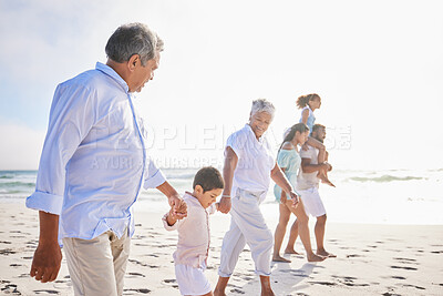 Buy stock photo Three generation family on vacation holding hands while walking along the beach together. Mixed race family with two children, two parents and grandparents spending time together by the sea