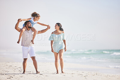 Buy stock photo Full length of a happy mixed race family walking along the beach and enjoying vacation. Adorable little sitting on her fathers shoulders while enjoying family time by the beach with her two parents