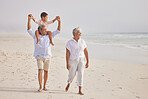 Happy mixed race grandparents walking on the beach with their grandson. Little boy sitting on his grandfathers shoulders and enjoying summer vacation by the beach