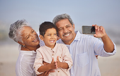 Buy stock photo Happy grandparents with grandson at the beach holding mobile and taking a selfie or video call with family during vacation by the sea. Adorable little boy smiling for picture with his grandmother and grandfather
