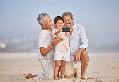 Buy stock photo Grandparents with grandson at the beach holding mobile and taking selfie or doing video call with family during vacation by the sea. Adorable little boy taking a picture with his grandmother and grandfather