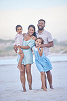 Full length portrait of a happy mixed race family standing together on the beach. Loving parents spending time with their two children during family vacation by the beach