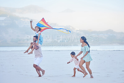 Buy stock photo Happy mixed race family running along the beach with a kite. Carefree parents and two children enjoying fun activity during family vacation by the sea