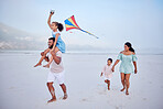 Happy mixed race family running along the beach with a kite. Carefree parents and two children enjoying fun activity during family vacation by the sea