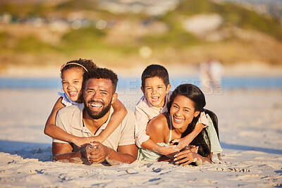 Buy stock photo Portrait of a happy mixed race family lying together on the beach. Little girl and boy lying on their parents while having fun and spending time together on vacation
