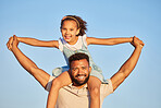 Happy loving father carrying his daughter on his shoulders while holding hands against blue sky. Adorable little girl on holiday with dad and enjoying family time