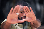One handsome young trendy african american man using his two hands to frame his face for a photograph in a city. Serious black man expressing with his hands up in protest against human rights downtown