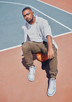 Full length handsome young trendy african american man sitting on a basketball alone on a court in the day. Fashionable and cool black man posing in a sports club. Hipster attitude and street culture