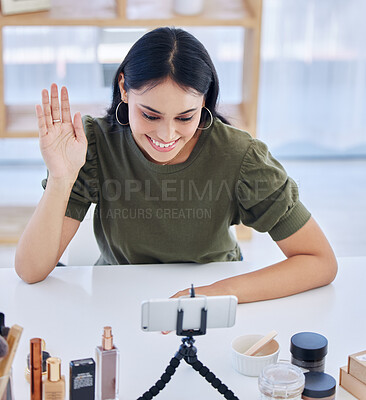 Hispanic beauty blogger waving at her smart phone while recording a video or broadcasting live. Beautiful young influencer sharing her beauty products and regime