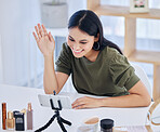 Smiling female beauty blogger waving at her smart phone while recording a video or broadcasting live. Beautiful young influencer sharing her beauty products and regime