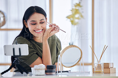 Young beauty blogger smiling while looking into a vanity mirror and doing a make-up tutorial while recording with her smart phone. Influencer sharing her beauty products and tips on social network