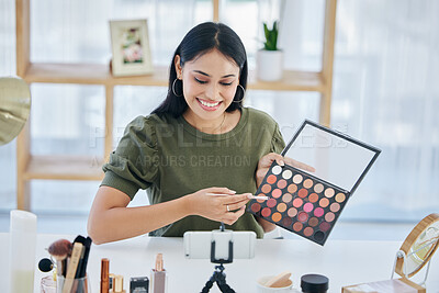 One beautiful mixed race creative woman sitting alone in a studio and using her cellphone to vlog while showing her eyeshadow palette. Happy hispanic makeup artist filming a tutorial for the internet