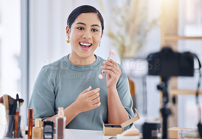 One beautiful young mixed race woman talking in a home studio and holding a rose quartz facial roller while using a camera to vlog a skincare routine tutorial. Smiling hispanic beauty expert blogging